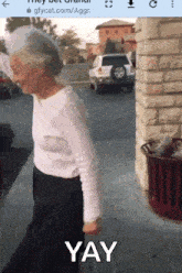 an elderly woman is walking down a sidewalk with the word yay written on the bottom