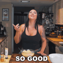 a woman in a black tank top is standing in a kitchen with a bowl of food and the words so good behind her