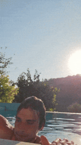 a man is laying in a pool with the sun shining through the trees