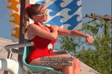 a woman in a red swimsuit and sunglasses is sitting in a chair .