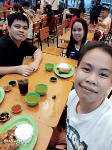 a group of people sitting at a table with plates of food and a phone that says ' oppo a57 ' on it