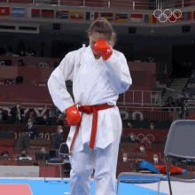 a woman in a white karate uniform with a red belt stands in front of a sign that says tokyo 2020