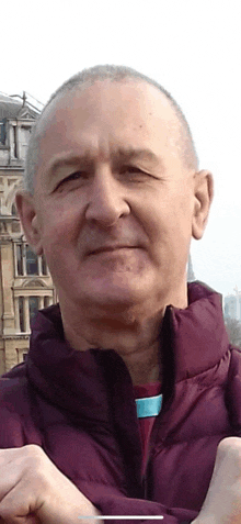 a man in a maroon jacket looks at the camera with a building in the background