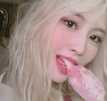 a blonde woman is eating a pink ice cream bar .