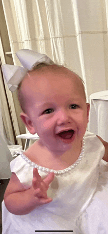 a baby wearing a white dress with pearls and a white bow on her head