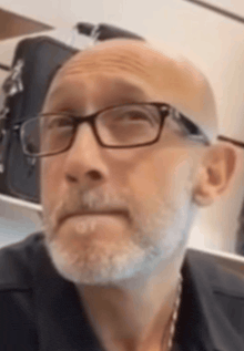 a bald man with glasses and a beard is looking at the camera