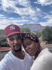 a man wearing a ny hat stands next to a woman wearing hoop earrings