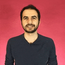 a man with a beard is standing in front of a pink background .