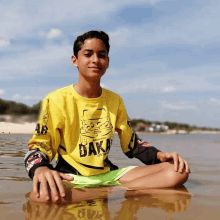 a boy is sitting in the water wearing a yellow shirt that says dakar