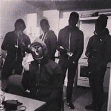 a group of men are standing in a kitchen wearing masks and hoodies .