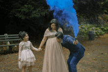 a man in a suit is holding a blue smoke bomb in front of a pregnant woman and a little girl