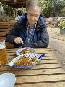 a man in a blue jacket is sitting at a table eating noodles