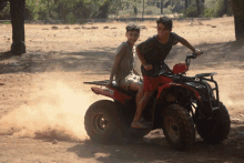 two young boys riding a red atv in the dirt