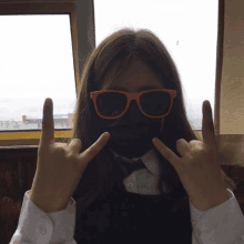 a girl wearing sunglasses and a black mask making a devil horns sign