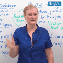 a woman in a blue shirt stands in front of a white board