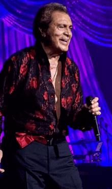 a man in a red and black shirt is singing into a microphone on a stage