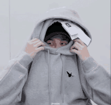 a person wearing a grey hoodie with a bird on it covering their face