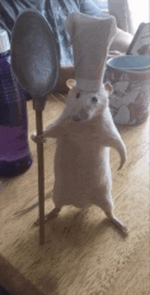 a stuffed rat wearing a chef hat is holding a wooden spoon .