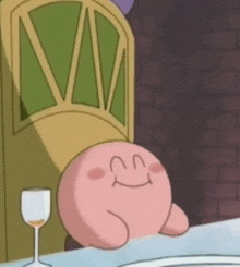 kirby is sitting at a table with a glass of wine and a chair .