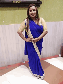 a woman in a blue and gold saree stands in front of a wall that says ytljawk