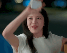 a woman in a white shirt is holding a glass of water in her hand .