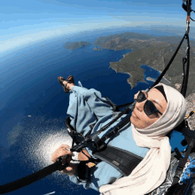 a woman wearing sunglasses and a hijab is flying a parachute over the ocean