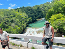 two men standing on a bridge overlooking a waterfall in the woods