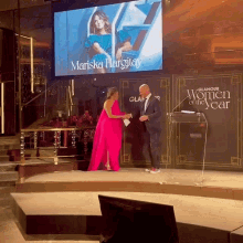 a woman in a pink dress is standing on a stage in front of a glamour women of the year banner