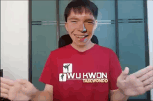 a man wearing a red wu kwon taekwondo shirt is smiling