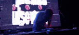 a man playing a keyboard in front of a screen that says ' us '