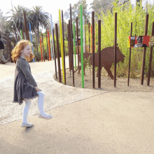 a little girl stands in front of a fence with a sign that says ' elephant ' on it