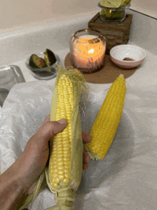 a person holding a corn on the cob in front of a candle