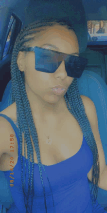 a woman wearing sunglasses and a blue tank top is sitting in the back seat of a car