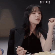 a woman sitting at a table with a netflix logo on the bottom right