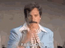 a man with a mustache is wearing a blue suit and a scarf and is saying fabulous .