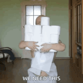 a man in a towel is holding a stack of toilet paper rolls and says " we need this "