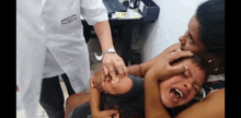 a woman is holding a child who is crying while a doctor is giving him a shot .