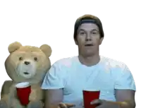 a man sitting next to a teddy bear holding a cup