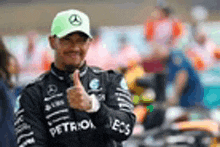 lewis hamilton is giving a thumbs up sign while wearing a green hat .