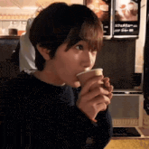 a woman drinking a cup of coffee in front of a sign that says ' cafe menu '