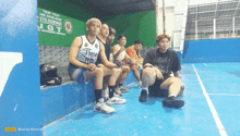 a group of basketball players sit on a bench in front of a sign that says ugt