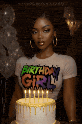 a woman wearing a birthday girl shirt stands in front of a cake with lit candles