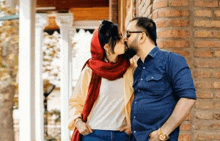 a man and woman kissing in front of a brick building