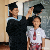 a woman in a graduation cap and gown is putting a hat on a girl in front of a blackboard that says welcome