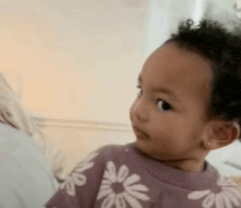a baby is wearing a purple sweater with white daisies on it .