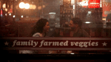 a man and woman are looking at each other in front of a sign that says " family farmed veggies "