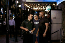 a man wearing a shirt that says security is standing next to a police officer