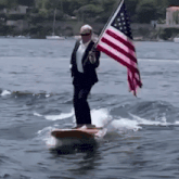 a man in a suit is holding an american flag while standing on a surfboard