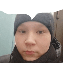 a young boy wearing a black beanie and a scarf looks at the camera