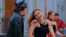 a woman in a black top is laughing with a man in a bandana behind her
